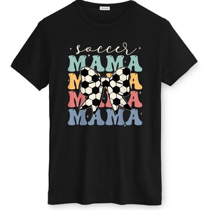 May include: Black t-shirt with a colorful graphic design. The design features the words "soccer mama" in a retro font, with a soccer ball bow in the center. The text is layered in blue, orange, pink, and teal.