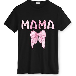 May include: Black t-shirt featuring the word "MAMA" in pink, patterned letters. A pink bow graphic is centered below the word. The shirt has a crew neck and short sleeves.