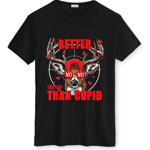 May include: Black t-shirt featuring a deer wearing a red cap and sunglasses, with the text "BETTER aim THAN CUPID" in red. The deer's antlers are adorned with red heart shapes, and the design is set against a white target.