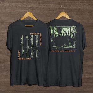 Könnte beinhalten: Schwarze T-Shirts mit Bandgrafik. Auf der Vorderseite des Shirts steht "TYPE O NEGATIVE" und "OCTOBER RUST" mit einem Dornen-Design. Auf der Rückseite des Shirts befindet sich ein Bandfoto und der Text "WE ARE THE VANDALS".