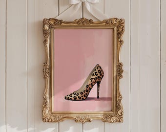 May include: A framed print of a high-heeled shoe with a leopard print design. The artwork is set against a pink background and framed in an ornate gold frame. A white bow hangs above the frame.