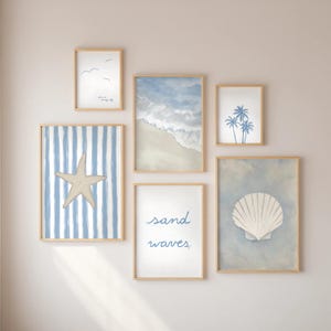 Pode incluir: Uma coleção de impressões de arte emolduradas com tema costeiro. As impressões apresentam imagens de estrelas do mar, ondas da praia, conchas e palmeiras em tons de azul e branco. A frase "sand waves" está escrita em uma das impressões.