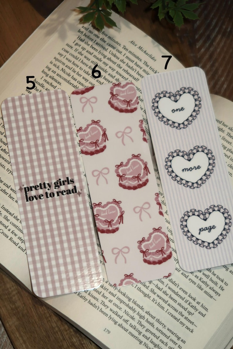 May include: Three decorative bookmarks with different designs. One bookmark has a pink gingham pattern with the text "pretty girls love to read." Another features heart-shaped designs with bows. The third has heart shapes with the words "one," "more," and "page."