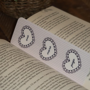 May include: Three heart-shaped bookmarks with the words "one", "more", and "page" printed on them. Each bookmark has a white heart with a scalloped border and a striped background.