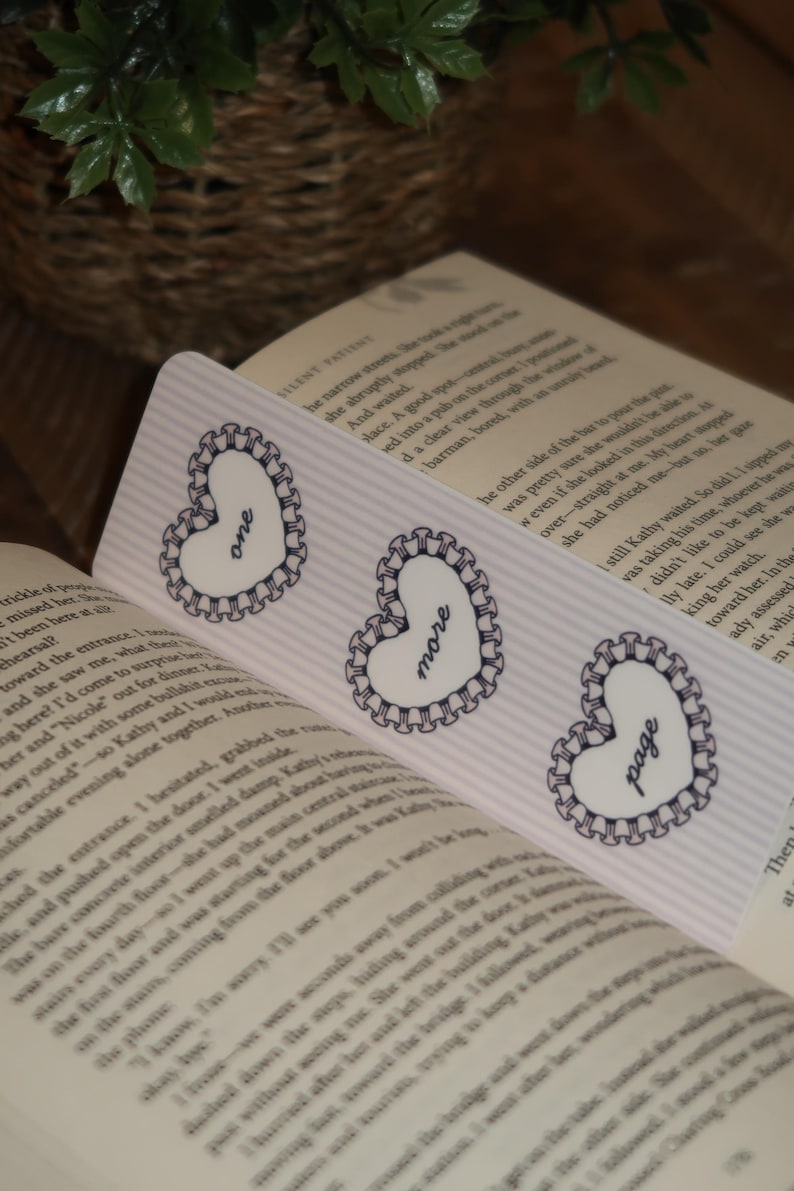 May include: Three heart-shaped bookmarks with the words "one", "more", and "page" printed on them. Each bookmark has a white heart with a scalloped border and a striped background.