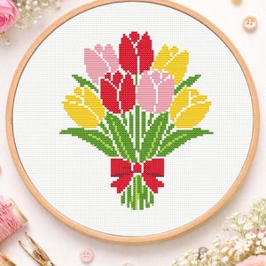 May include: A cross-stitch embroidery of a bouquet of tulips in a wooden hoop. The tulips are red, pink, and yellow, with green leaves and a red bow. The embroidery is on white fabric.