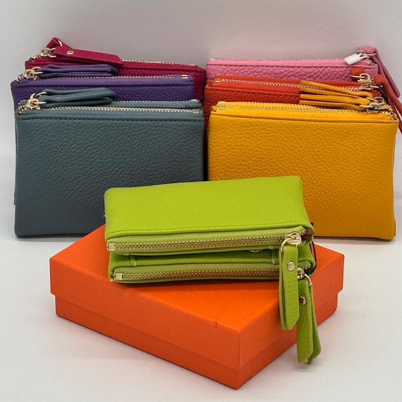 K&ouml;nnte beinhalten: Eine Sammlung rechteckiger Rei&szlig;verschlusstaschen in verschiedenen Farben, darunter Limettengr&uuml;n, Gelb, Orange, Pink, Violett, Magenta und Schieferblau. Jede Tasche hat eine strukturierte Oberfl&auml;che, goldfarbene Metallrei&szlig;verschl&uuml;sse und passende Lederzipper.