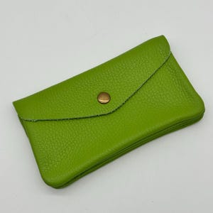 May include: A lime green leather wallet with a textured surface. The wallet has a flap closure secured by a gold-colored snap. The wallet is rectangular and appears to be folded.