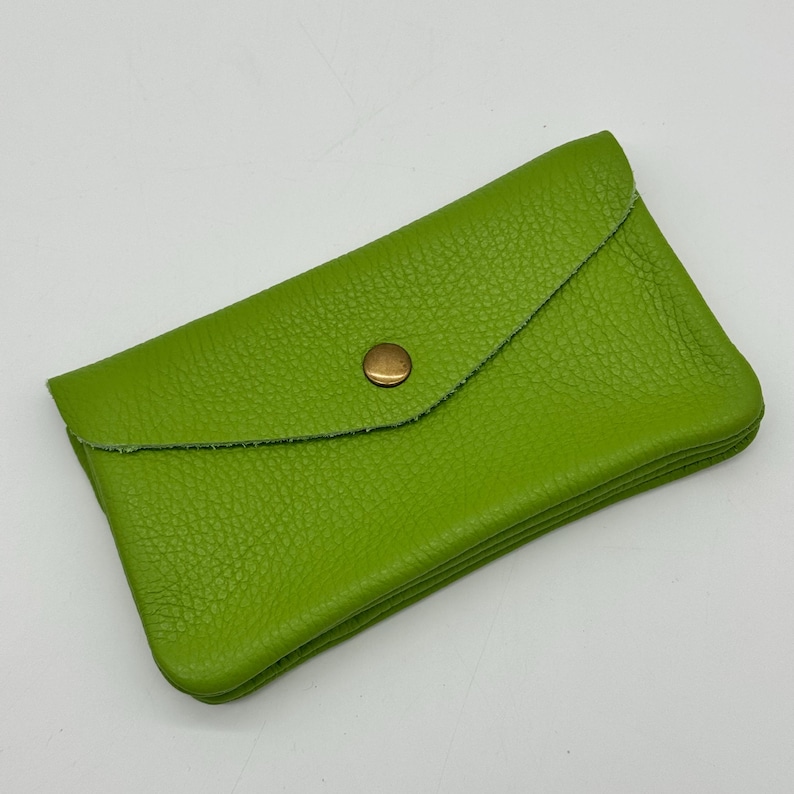 May include: A lime green leather wallet with a textured surface. The wallet has a flap closure secured by a gold-colored snap. The wallet is rectangular and appears to be folded.