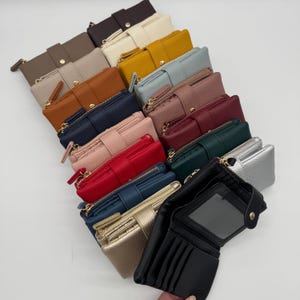 May include: A collection of bi-fold wallets in various colours including black, gold, blue, red, pink, green, burgundy, brown, tan, grey, white, and dark brown. Each wallet features a textured finish, a snap button closure, and a zippered compartment.