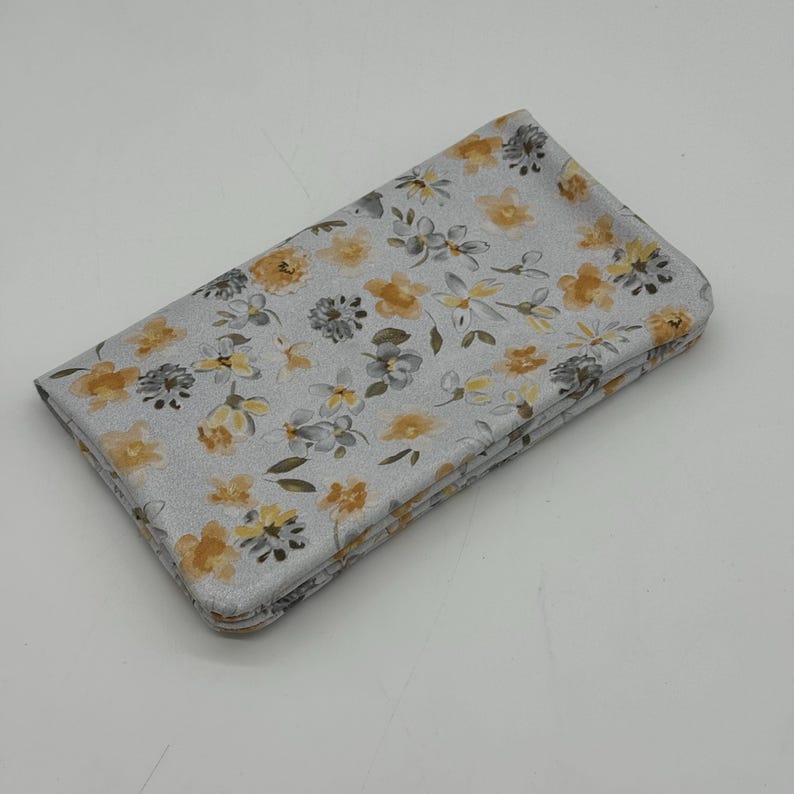 May include: Folded fabric with a floral pattern. The fabric is light gray with yellow, gray, and green floral designs. The flowers are in various sizes and shapes, creating a delicate and intricate pattern.