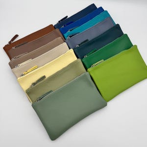 May include: A collection of rectangular zipped pouches arranged in a fan pattern. The pouches feature a textured surface and come in a variety of colours including brown, tan, beige, yellow, olive, sage green, bright green, dark green, grey, teal, and blue.