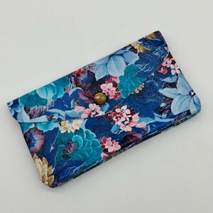 May include: A blue floral clutch with a brass button closure. The clutch features a pattern of blue, pink, and cream-colored flowers on a dark blue background. The clutch is rectangular and has a flap closure.
