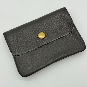 May include: A dark gray leather wallet with a textured surface. The wallet has a flap closure secured by a gold-colored button. The edges of the wallet are raw and unfinished.