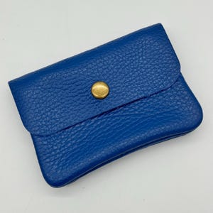 May include: A small, cobalt blue leather wallet with a textured surface. The wallet has a flap closure secured by a gold-colored snap. The wallet is rectangular and appears to be empty.