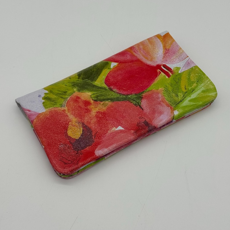 May include: A rectangular wallet with a floral design. The wallet features a vibrant pattern of red and pink flowers with green leaves against a light background. The wallet is closed and appears to be made of a smooth material.