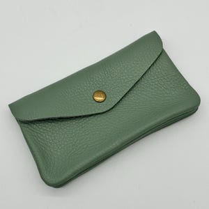 May include: A sage green leather wallet with a flap closure and a brass button. The wallet has a textured surface and a rectangular shape. The design is simple and elegant, suitable for carrying cards and cash.
