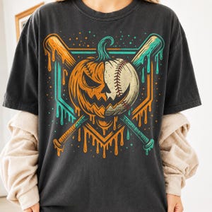 Może przedstawiać: Ciemnoszary t-shirt z kr&oacute;tkim rękawem z nadrukiem graficznym przedstawiającym hybrydę dyni i piłki baseballowej. Wz&oacute;r zawiera dwa skrzyżowane kije baseballowe z efektem ściekania w kolorze pomarańczowym i morskim na tle geometrycznej bazy.