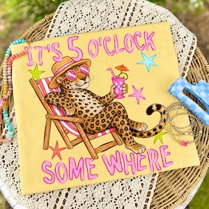 Puede incluir: Cojín decorativo amarillo con un leopardo con gafas de sol y sombrero, relajándose en una tumbona, sosteniendo una bebida rosa. El texto "IT'S 5 O'CLOCK SOMEWHERE" está en rosa, con estrellas.