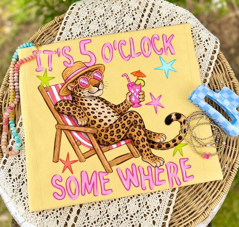 Op de afbeelding: Geel sierkussen met een luipaard met zonnebril en hoed, ontspannen in een strandstoel, met een roze drankje. De tekst "IT'S 5 O'CLOCK SOMEWHERE" staat in roze letters, met sterren.