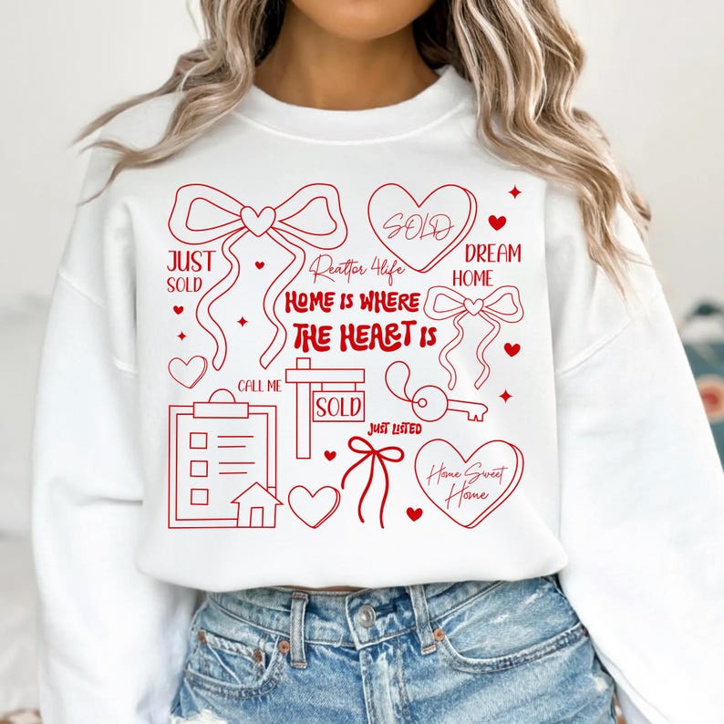 May include: White sweatshirt with red graphic elements related to real estate. The design includes bows, hearts, a key, and the phrases "Just Sold," "Home is Where the Heart Is," and "Home Sweet Home."