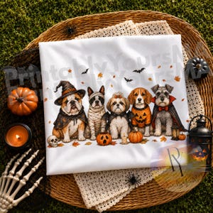 May include: A white t-shirt featuring a graphic illustration of five dogs dressed in Halloween costumes, including a bulldog in a witch hat, a mummy dog, a dog with bat wings, a beagle in a pumpkin sweater, and a schnauzer in a vampire cape.