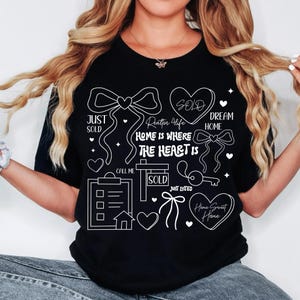 May include: Black t-shirt with white line art featuring bows, hearts, and text. Text includes "Just Sold," "Realtor 4 Life," "Home is Where the Heart Is," "Dream Home," and "Home Sweet Home." A key, house, and checklist are also shown.