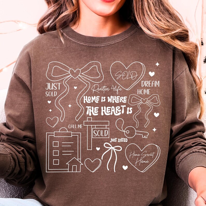 May include: Brown sweatshirt with white graphic elements related to real estate. The design includes hearts, bows, a key, a house, and the words "SOLD", "JUST SOLD", "DREAM HOME", "HOME IS WHERE THE HEART IS", "JUST LISTED", "Home Sweet Home", and "Realtor 4 Life".