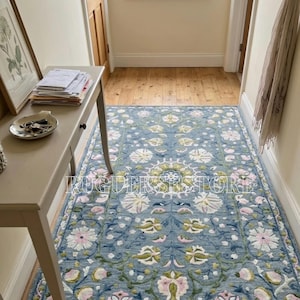 May include: A rectangular blue rug with a floral pattern in a hallway. The rug features white, pink, and green floral designs. The rug is placed on a wooden floor, and the hallway has light-colored walls.