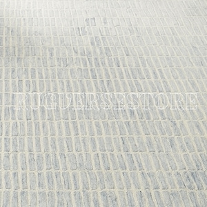 Puede incluir: Una alfombra rectangular con un patrón texturizado de rectángulos azul claro y blanco roto. El diseño crea un efecto geométrico sutil, adecuado para varios estilos de interior. El texto "RUGUERSESTORE" es visible.