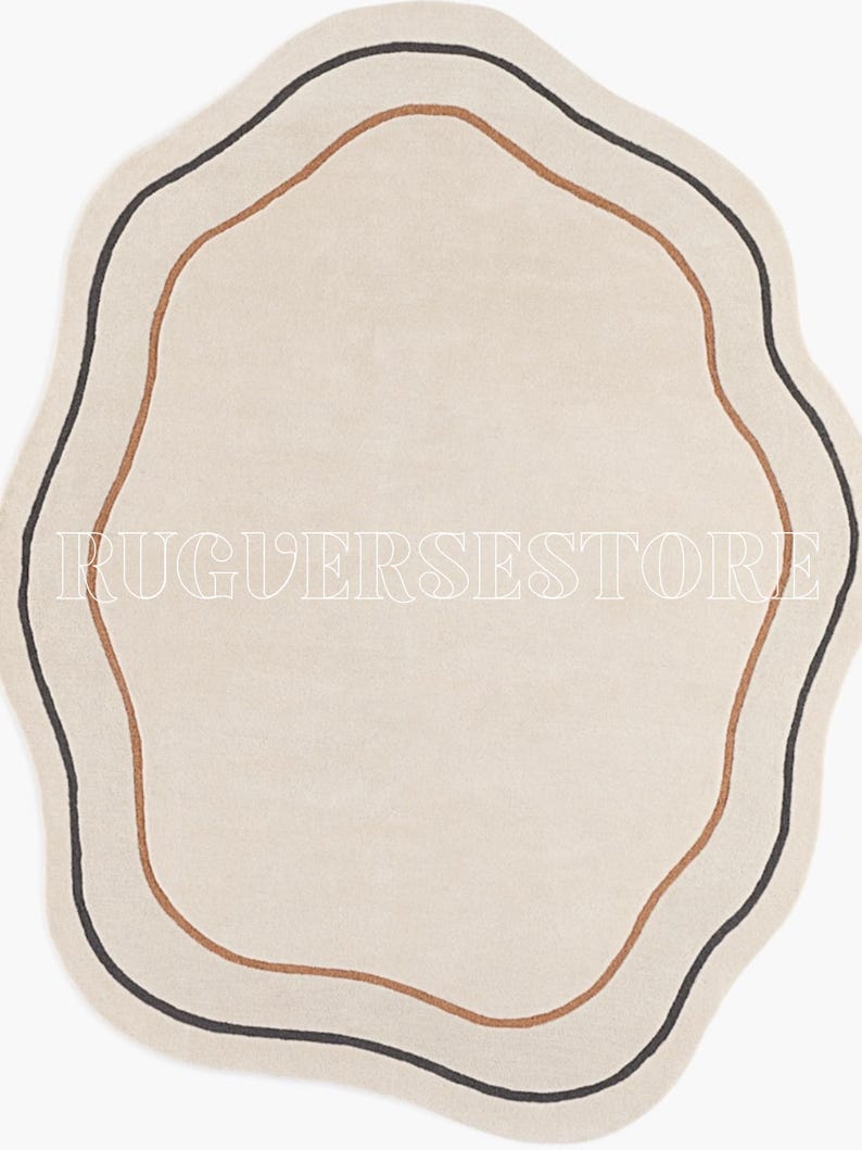 May include: A cream-coloured, wavy-edged rug with a minimalist design. It features two concentric lines: a dark brown outer line and a lighter brown inner line. The text "RUGVERSESSTORE" is printed in white across the rug.