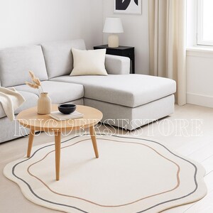 May include: A cream-coloured, wavy-edged rug with brown and grey border lines. The rug is in a living room with a light-coloured sofa, wooden coffee table, and vase. The room has a minimalist design. The rug's shape is irregular.