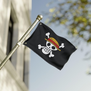 May include: A black flag with a white skull and crossbones design, wearing a straw hat with a red band. The flag is mounted on a gold pole and is waving in the wind against a blue sky.