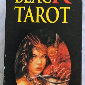 May include: A black Tarot card box with the title "THE BLACK TAROT" in yellow lettering. The image on the box depicts a woman with dark hair and a red, demonic figure. The overall design has a fantasy theme.