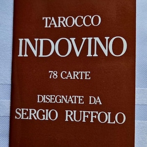 Puede incluir: Un folleto rectangular con una cubierta de color marrón oscuro que presenta texto en blanco que dice DAL NEGRO TAROCCO INDOVINO 78 CARTE DISEGNATE DA SERGIO RUFFOLO NOTE ESPLICATIVE. El folleto sirve como guía explicativa para un mazo de tarot.