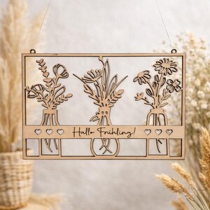 Könnte beinhalten: Rechteckiges Wandbild aus hellem Holz mit ausgeschnittenem Design von drei Vasen mit Blumen. Der Schriftzug "Hallo Frühling!" ist vorhanden. Das Dekor ist aus hellem Holz gefertigt und hat eine natürliche Oberfläche.