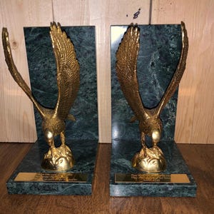 May include: A pair of bookends featuring gold-toned eagles with wings spread, mounted on dark green marble bases. Each base includes a rectangular gold plaque with engraved text referencing Isaiah 40:31, depicting eagles in flight.