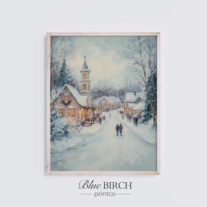 Könnte beinhalten: Gerahmtes Winterlandschaftsgemälde, das eine verschneite Dorflandschaft darstellt. Das Kunstwerk zeigt eine Kirche mit Turm, Häuser und Figuren auf einer verschneiten Straße. Die Farbpalette umfasst Weiß-, Blau- und warme Gelbtöne. Der Text "Blue Birch printco" befindet sich unten.