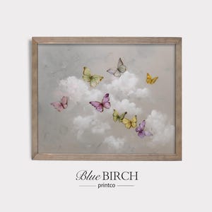 May include: A framed print featuring a dreamy scene of butterflies in flight. The artwork showcases pastel-colored butterflies, including pink, yellow, and purple, amidst fluffy white clouds against a soft gray background. The frame is a light brown color, and the text "Blue Birch printco" is at the bottom.