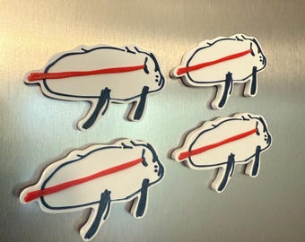 May include: Four white, cartoonish buffalo-shaped magnets with a red stripe across the body and dark blue outlines. The magnets have dark blue legs and are arranged on a silver surface.