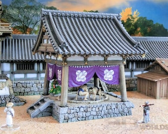 May include: Miniature Japanese sumo wrestling ring with a gray tiled roof, purple curtains, and stone walls. Two sumo wrestlers are in the ring. A figure in a white outfit stands nearby. The scene is set in a traditional Japanese village.
