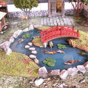 Peut inclure: Scène de jardin japonais miniature avec un pont rouge au-dessus d'un étang. L'étang présente des carpes koï, des nénuphars et des pierres de gué. La scène comprend un bâtiment traditionnel et une petite statue de cerf.