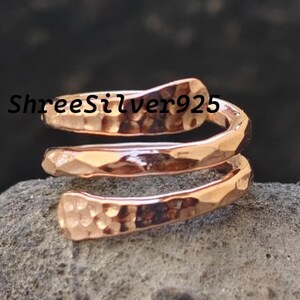 May include: A hammered copper-colored ring with a spiral design. The ring is made of metal and has a textured surface. The ring is displayed on a gray stone surface. The text "ShreeSilver925" is visible.