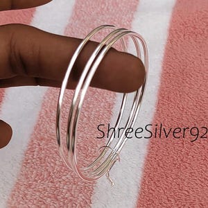 May include: Three silver hoop earrings, each with a thin, circular design and a polished, reflective finish. The text "ShreeSilver92" is visible. The earrings are presented against a pink and white striped backdrop.