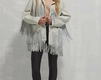 May include: A light-colored jacket with long fringe detailing. The jacket has a collared neckline, pockets, and long sleeves. The model is wearing black leggings and sunglasses.
