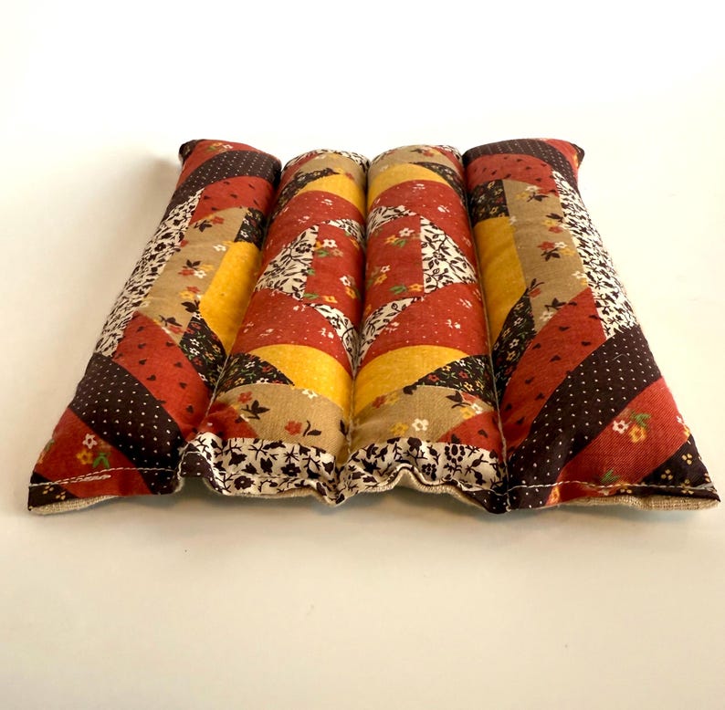 May include: Four rectangular, quilted fabric items with a patchwork design. The colour palette includes shades of red, brown, yellow, and beige. The fabric is patterned with floral and polka dot motifs. The edges are finished with a ruffled trim.