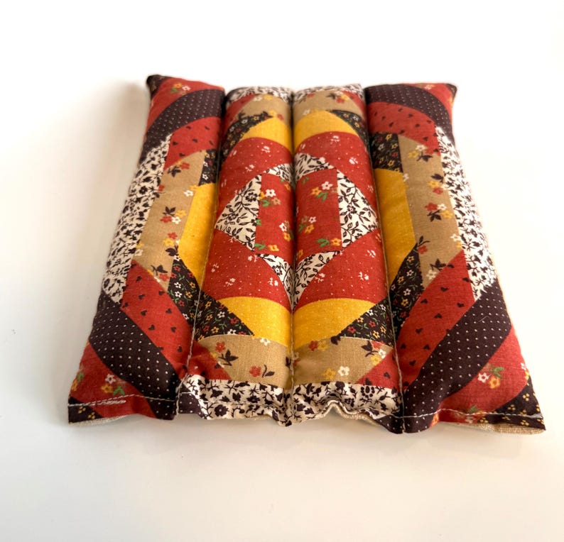 May include: A rectangular patchwork pillow in red, brown, yellow, and beige. The pillow is divided into four sections, each with a unique pattern, including floral and polka dot designs. The edges are finished with a floral trim. The pillow is made of fabric.