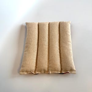 May include: A beige rectangular heating pad with four vertical quilted sections. The pad is made of a textured fabric and is designed for therapeutic use. The edges are slightly frayed, and the pad is centered on a white surface.