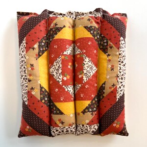 May include: A patchwork cushion with a vibrant design. The cushion showcases a central square of red and white floral fabric, framed by yellow, red, and brown patterned sections. The edges are finished with a floral print fabric.