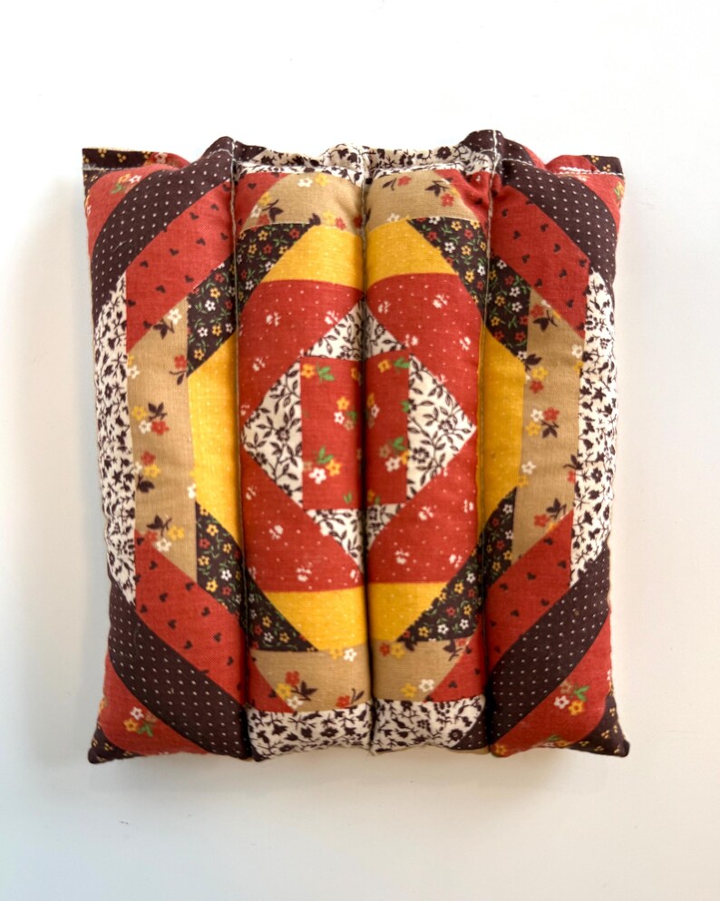 May include: A patchwork cushion with a vibrant design. The cushion showcases a central square of red and white floral fabric, framed by yellow, red, and brown patterned sections. The edges are finished with a floral print fabric.